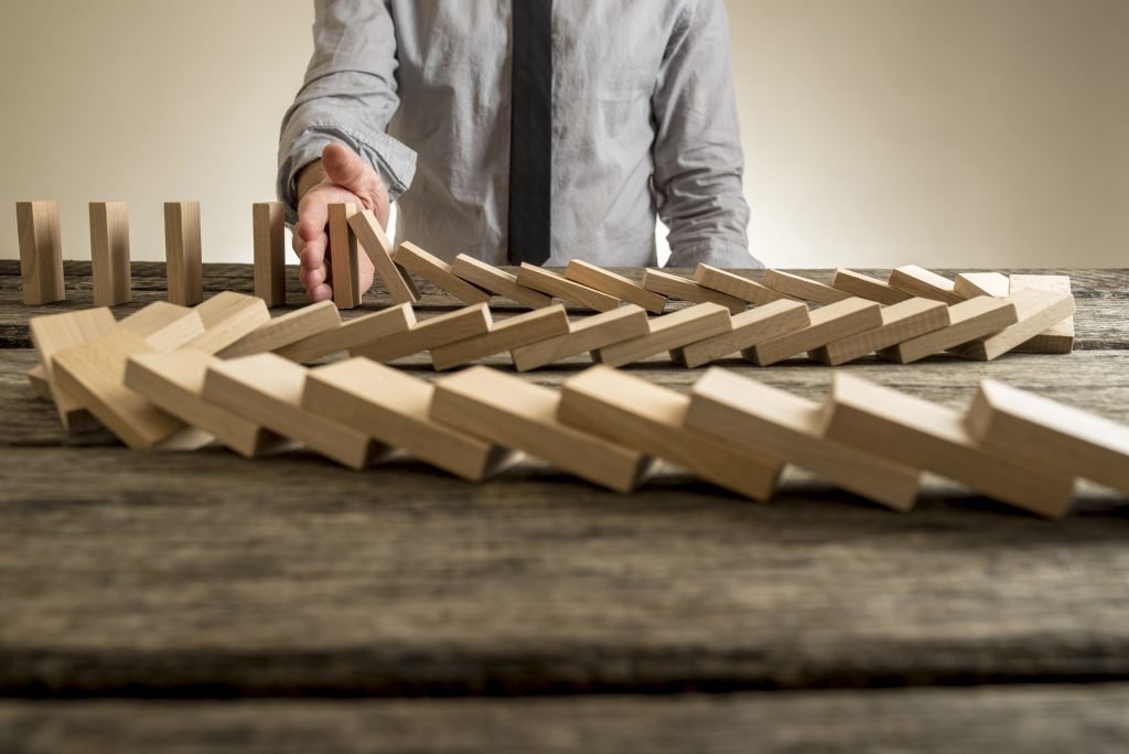 Hand stopping domino effect of wooden blocks